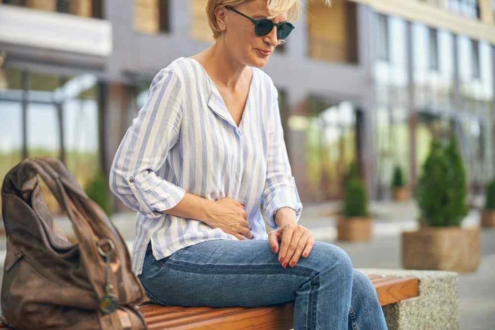 Femme assise sur un banc ayant des crampes intestinales