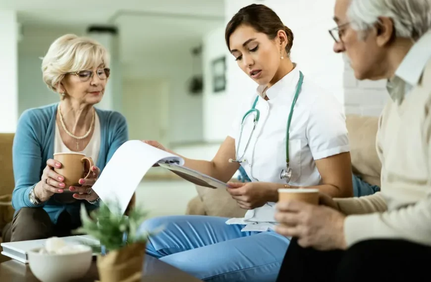 Une soignante explique la stomie digestive à un couple de personnes âgées assis dans leur salon