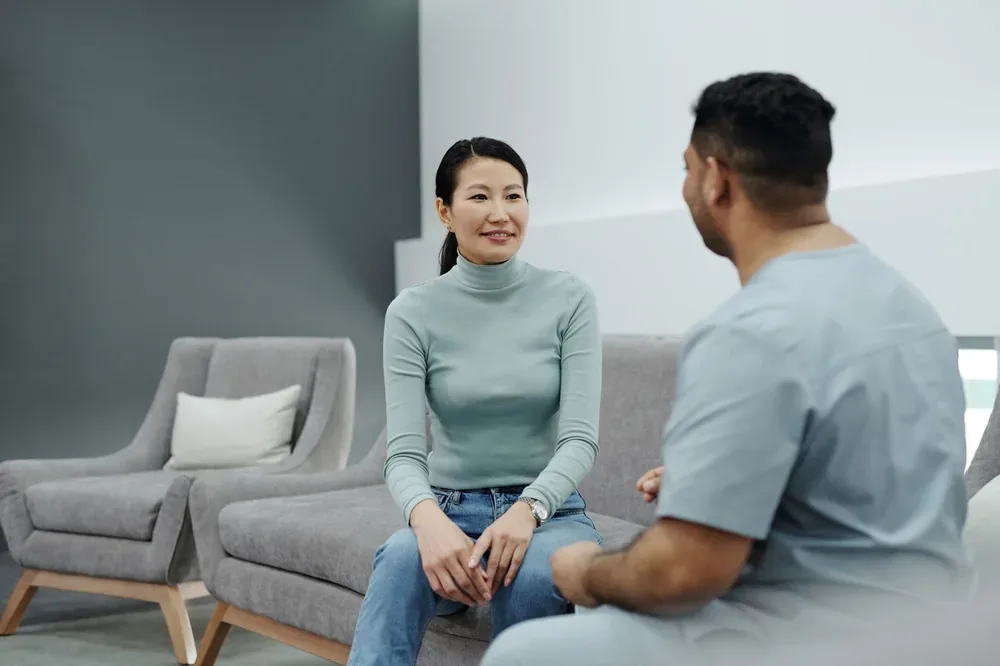 Femme assise sur un canapé échangeant avec un professionnel de santé en tenue médicale