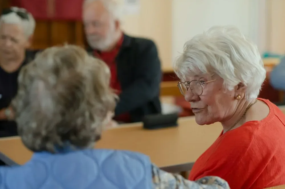 Pour illustrer la logorrhée, deux femmes âgées discutent à une table entourées d'autres personnes.