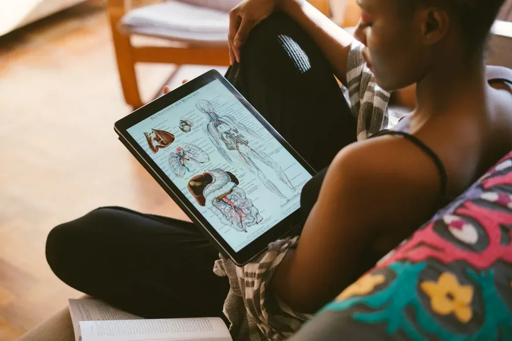 Femme consultant des planches anatomiques du corps humain sur une tablette.