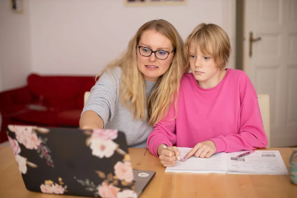Femme aidant un adolescent concentré à travailler sur un cahier devant un ordinateur portable