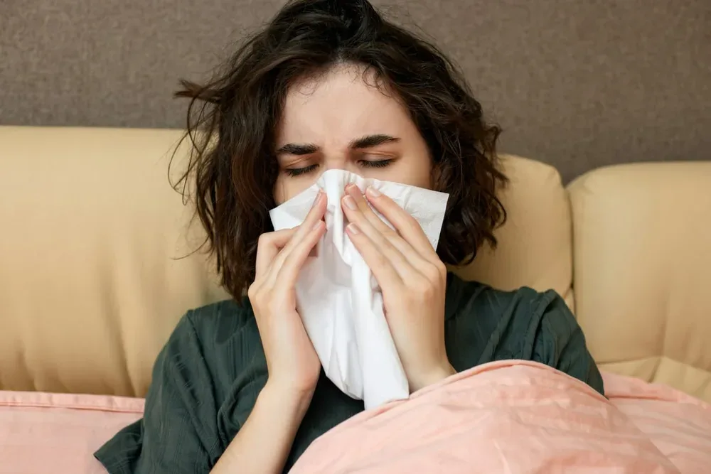 Allergie aux acariens : une femme éternue et se couvre le nez avec une serviette en papier.