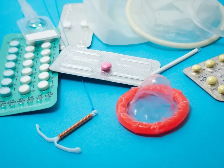 Assortiment de contraceptifs sur fond bleu, avec plaquettes, préservatifs et DIU.