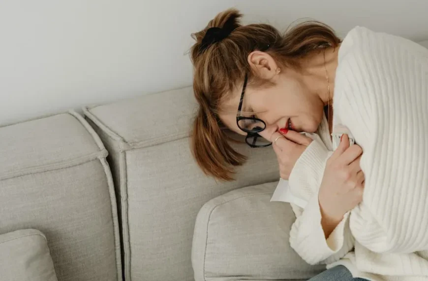 Emphysème pulmonaire : une femme assise sur un canapé porte une main à sa bouche et tient ses lunettes.