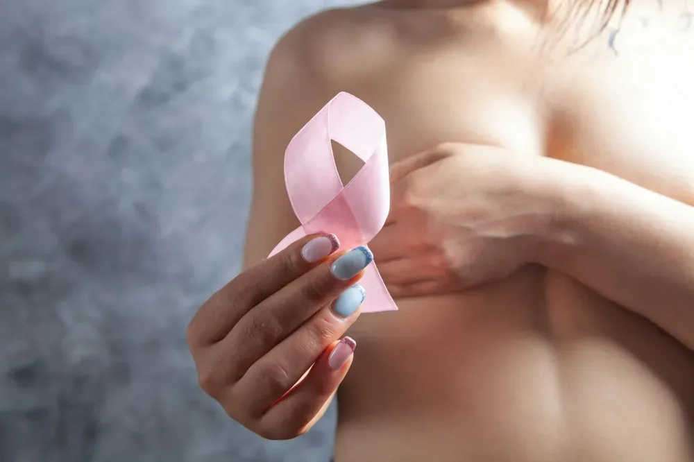 Une femme tient un ruban octobre rose entre ses doigts.