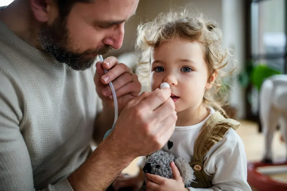 Père utilisant un mouche-bébé auprès d’une petite fille à la maison