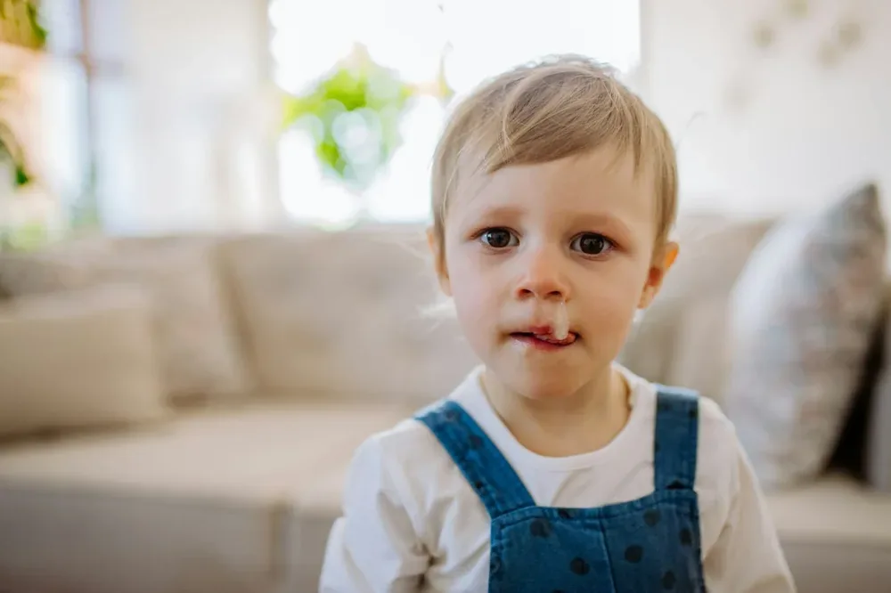 Petite fille avec un écoulement nasal, assise dans une pièce lumineuse
